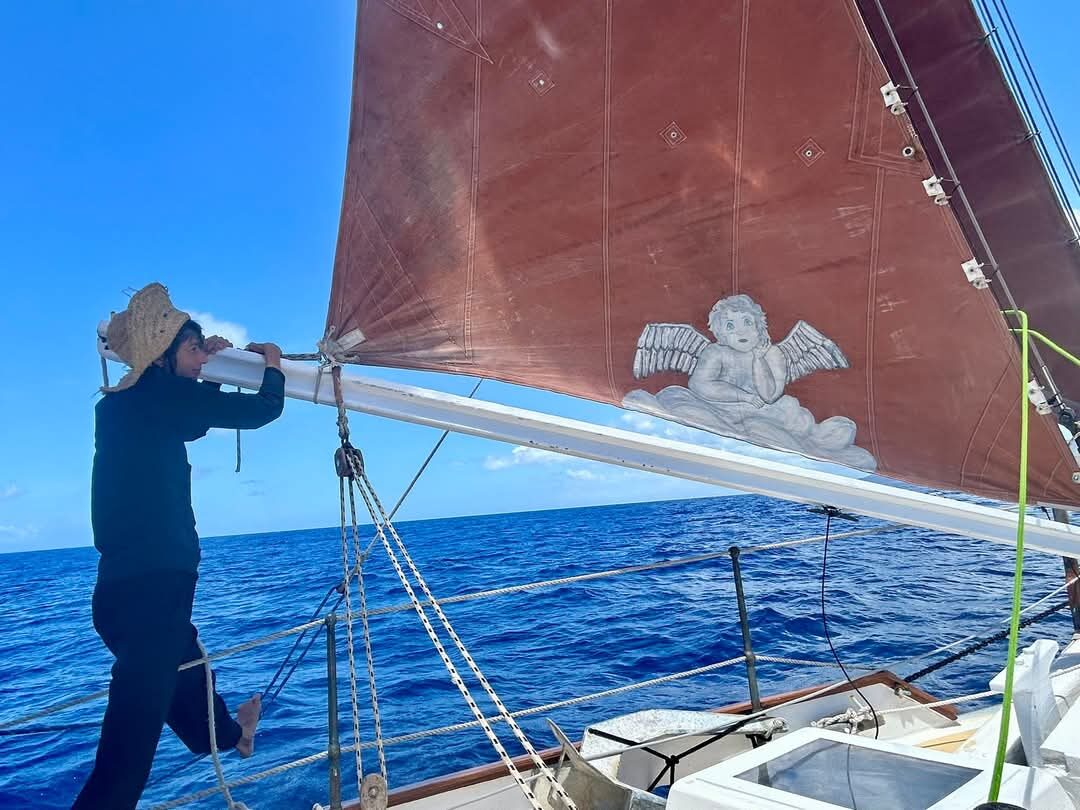 Angie Wolf at the bow of Cherub, straw hat, at sea