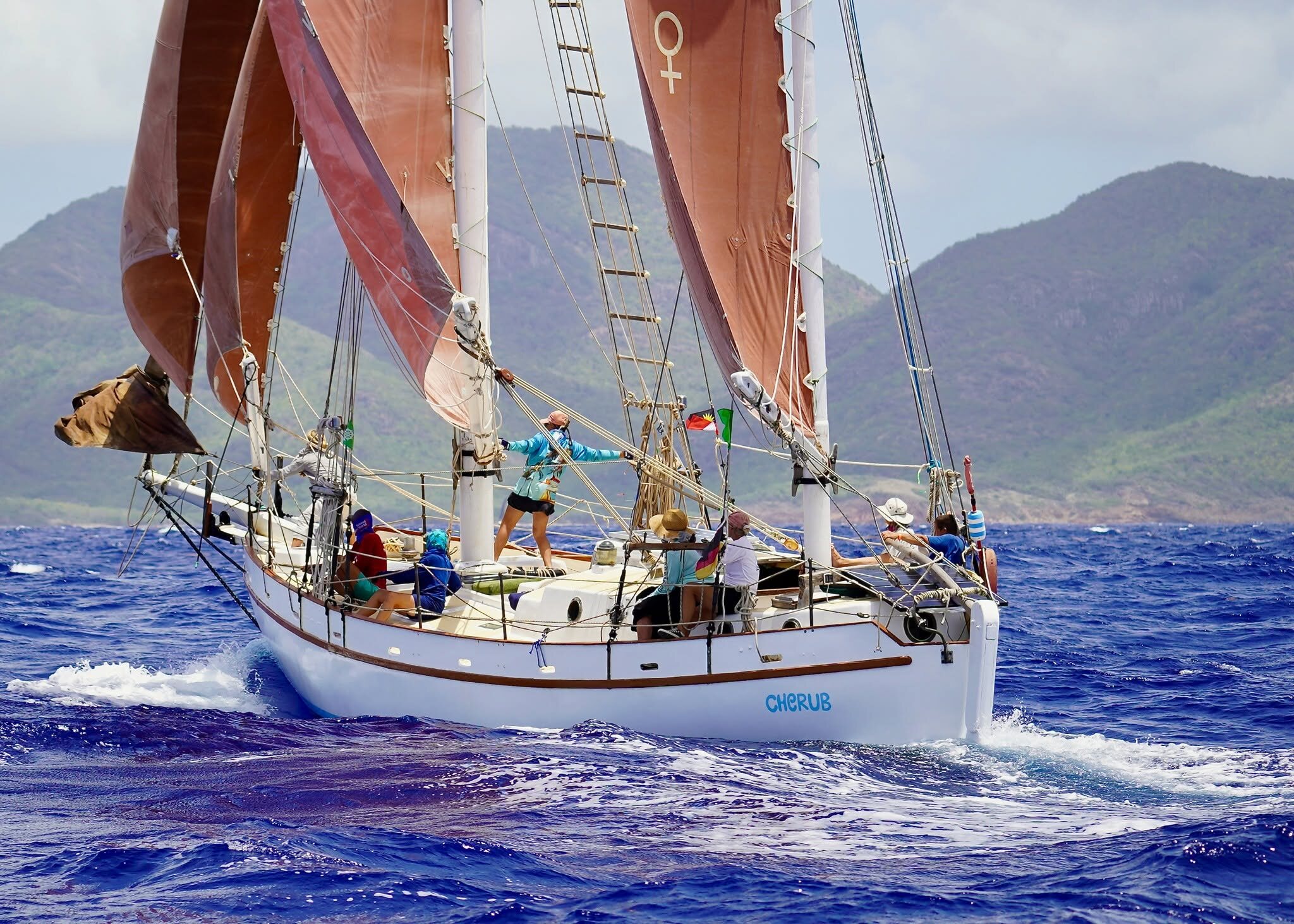 Cherub sailing hard under her tan sails, all-female crew on deck, at the Antigua Classics